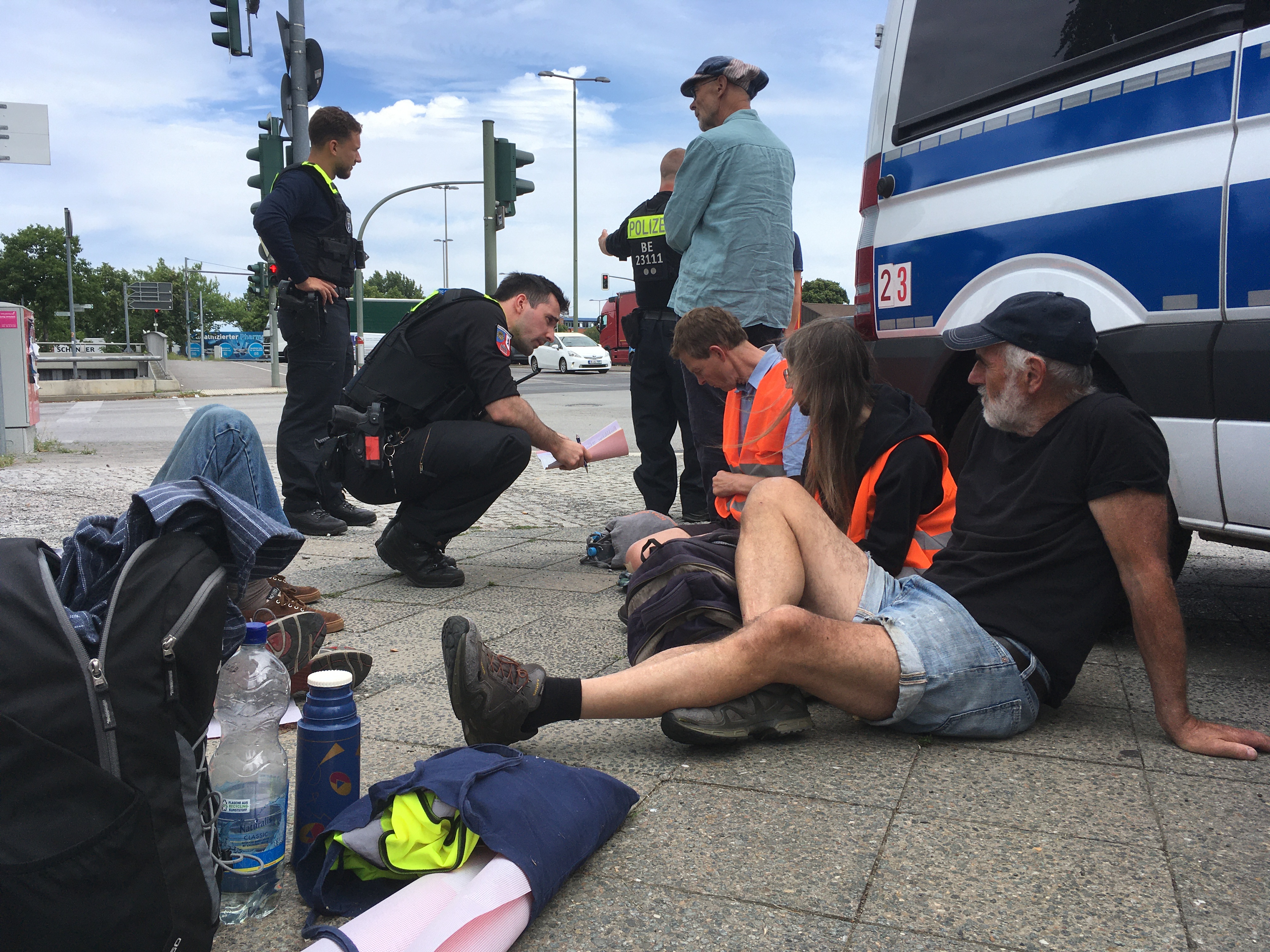 Menschen sitzen neben einem Polizeiauto auf dem Boden.